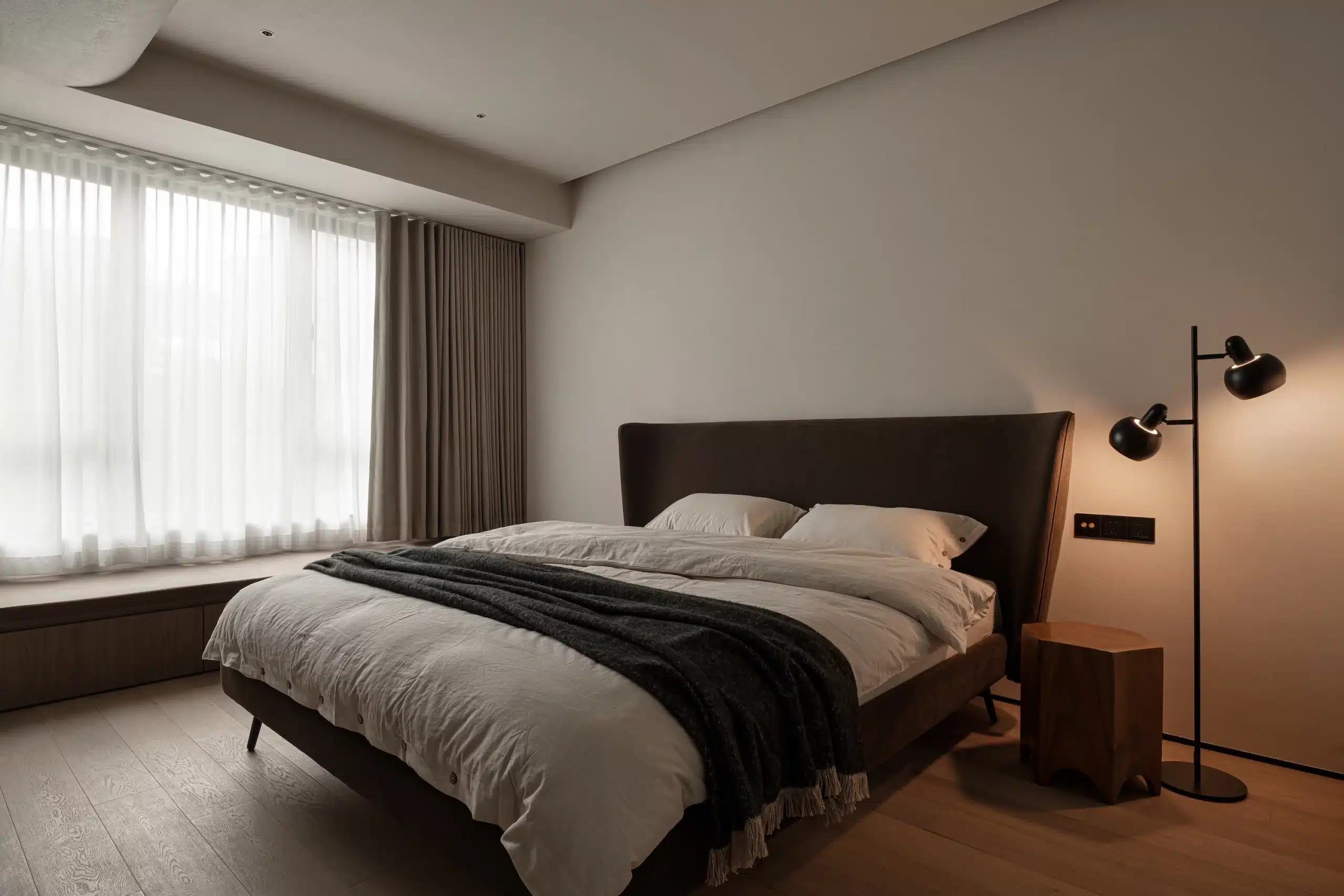 Japandi 臥室設計:架高木地板與洗水亞麻寢具的低重心配置,角落擺放落地燈散發柔光,展現溫潤安穩的北歐侘寂美學。