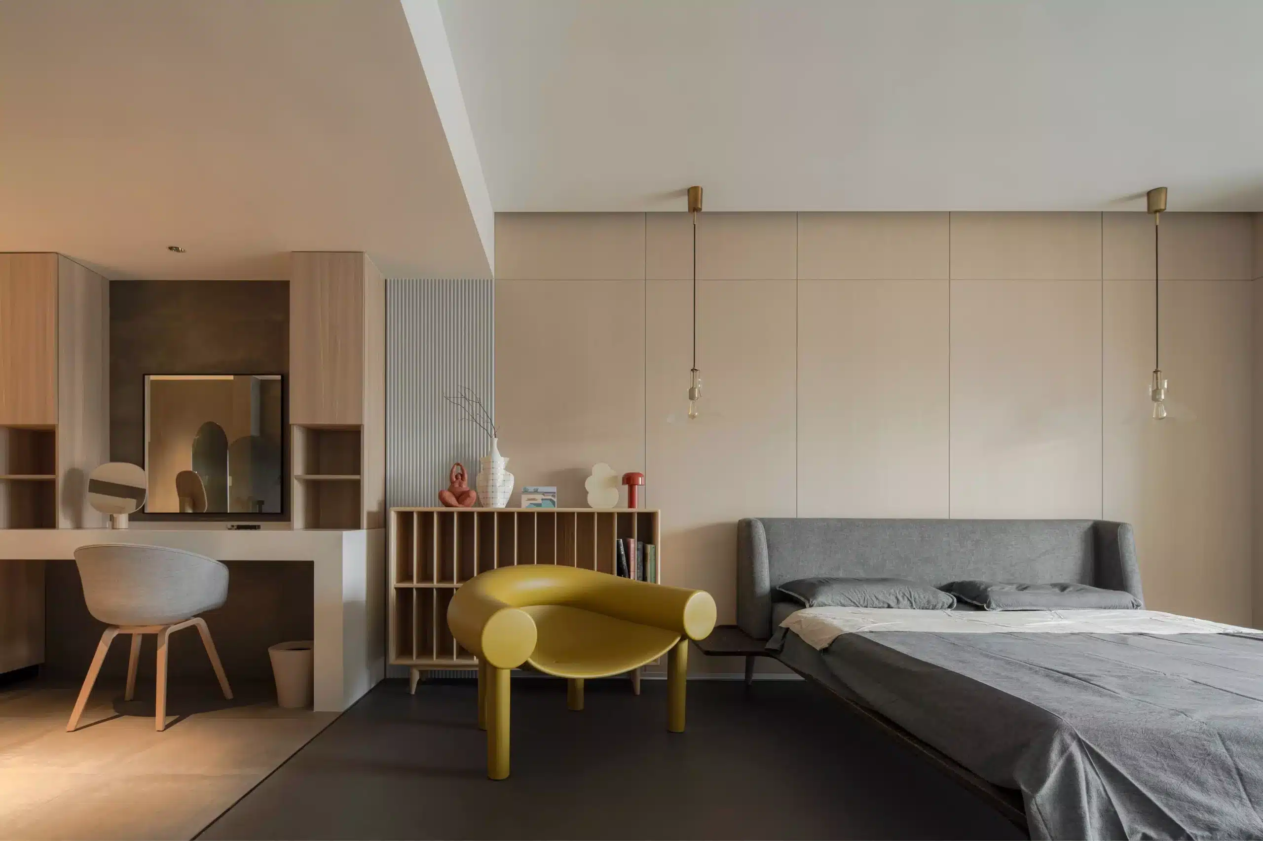 侘寂風臥室空間，灰色軟墊床頭背靠整面木質牆板，室內點綴一具幾何造型的黃色藝術單椅，展現現代美學與禪意的碰撞。