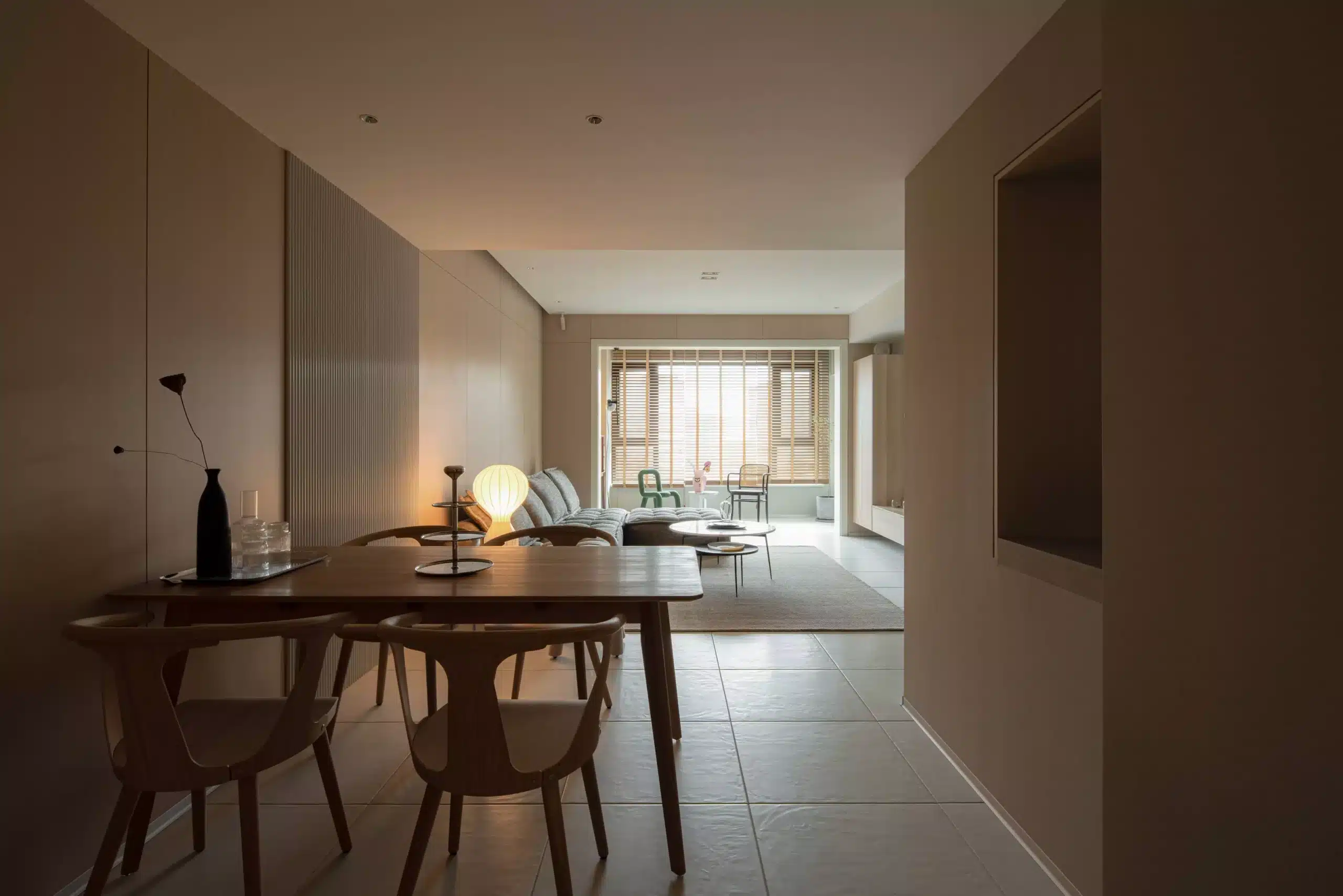 從餐廳視角望向客廳，實木餐桌與木質天花板相互呼應，窗邊採用木質百葉簾，展現 Japandi 風格中細膩的光影變化。