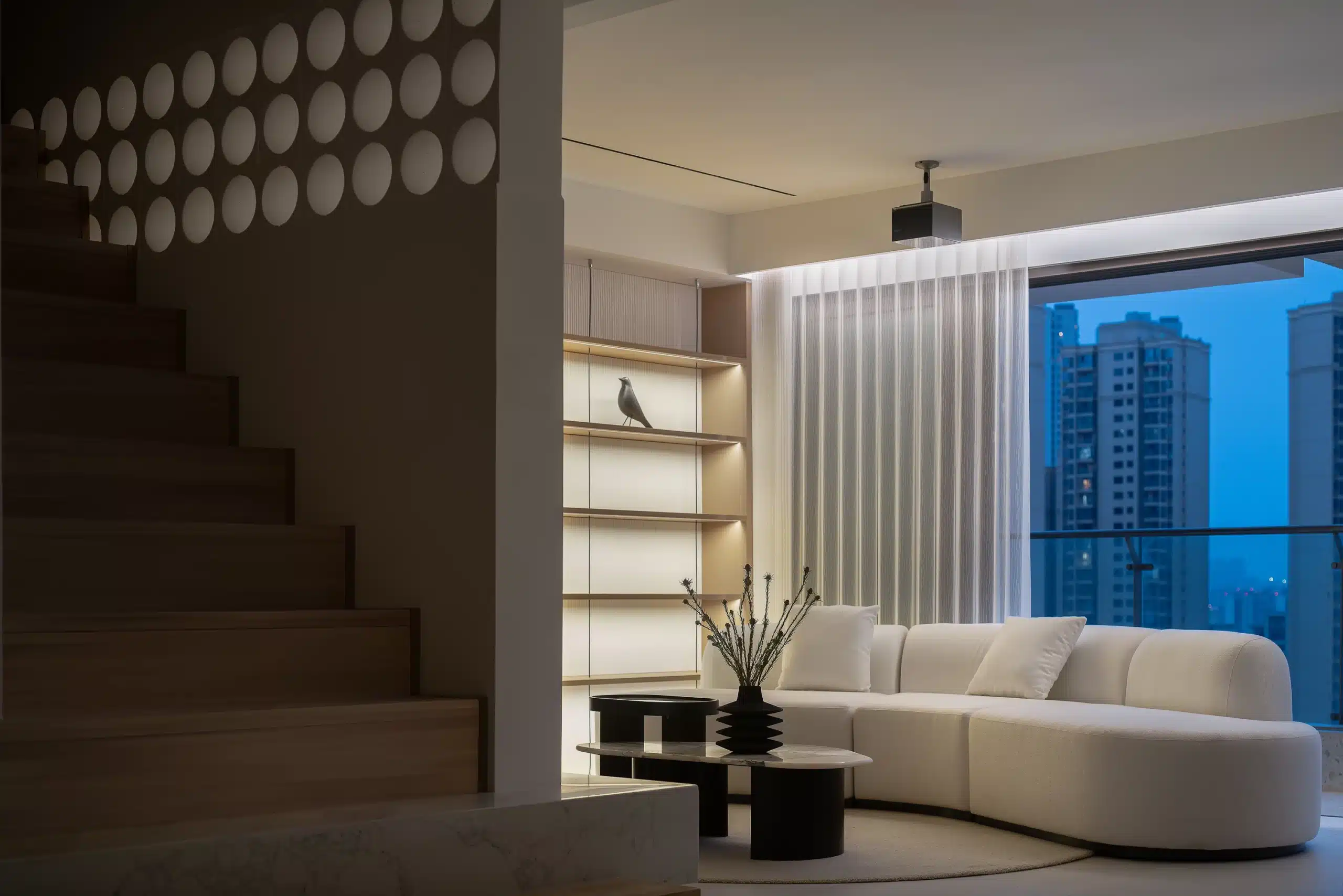 精品風客廳設計，運用具有建築感的圓形孔洞牆面作為場域區隔，搭配有機線條的白色弧形沙發與極簡投射燈光。